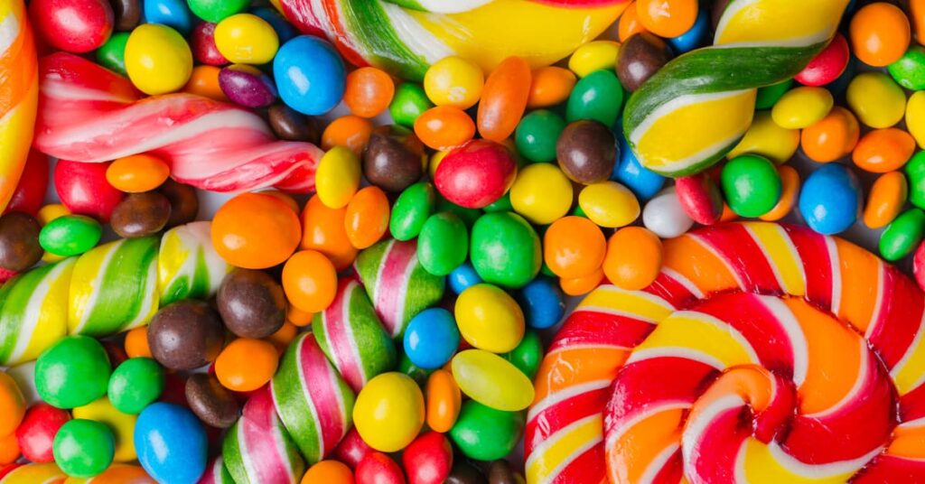 Grageas de colores junto a caramelos y piruletas en una composición de golosinas variadas